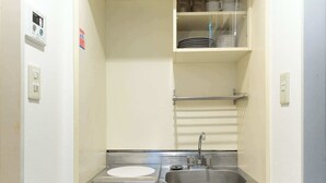 A compact kitchenette with a stainless steel sink, a small countertop, and a dish rack. - Sakura Yoyogi by Tranova (Tokyo)