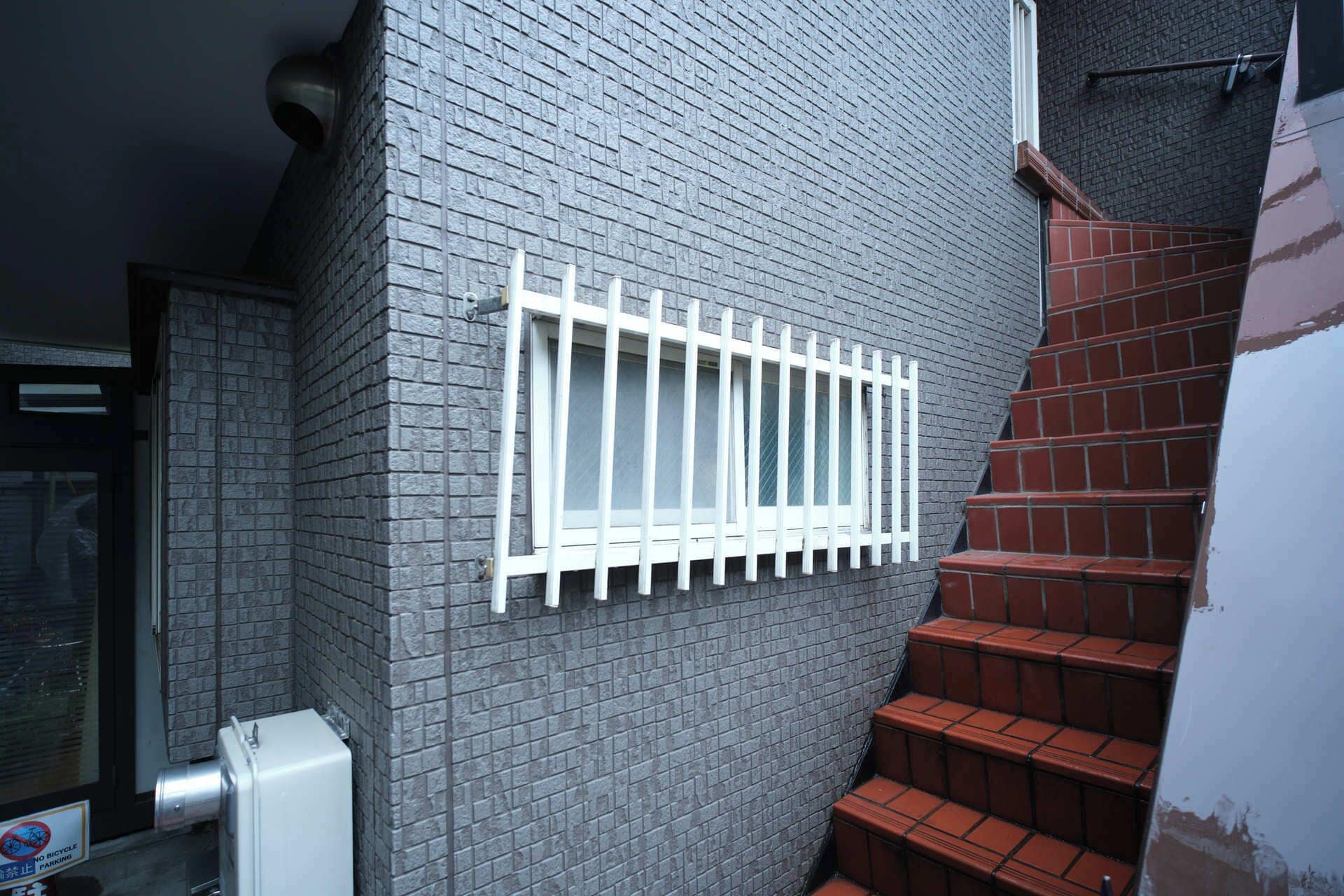 A brick wall with a barred window and a staircase with red steps.