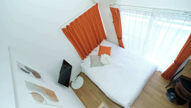 A modern hotel room with a large bed, orange curtains, a round side table, and a wooden floor. - Sakura Yoyogi by Tranova (Tokyo)