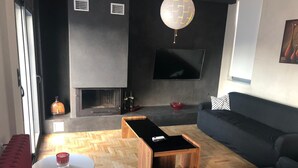 A modern living room with a fireplace, a sofa, a coffee table, and a TV mounted on the wall. - Luxurious Apartment With big Balcony Best Location (Athens)