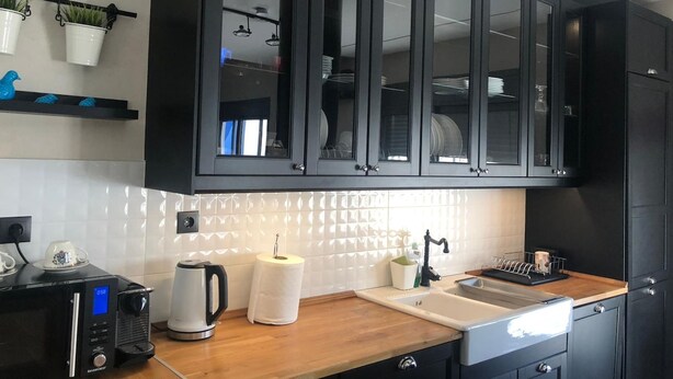 A modern kitchen with black cabinets, a wooden countertop, a kettle, a coffee maker, and a dish rack. - Luxurious Apartment With big Balcony Best Location (Athens)