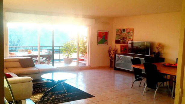 Uma sala de estar com sofá, mesa de centro, televisão e um canto de jantar com cadeiras e mesa.
