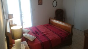 Quarto com cama, mesa de cabeceira com abajur, cadeira e janela com cortinas.