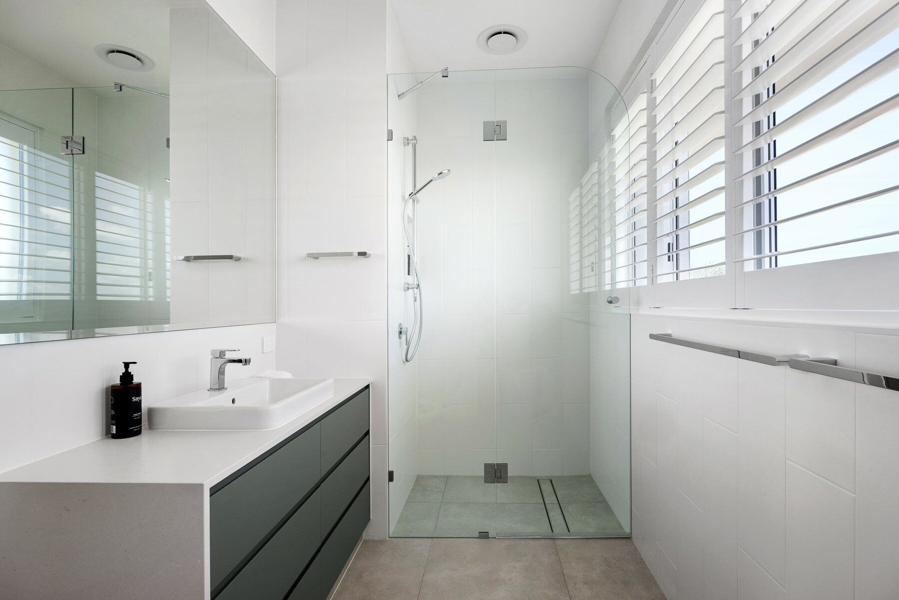 A modern bathroom with a glass shower enclosure, a white sink, and a large mirror.