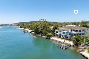 A waterfront property with a multi-story building, dock, and surrounding greenery. - River's Edge At Mariners (Noosa)