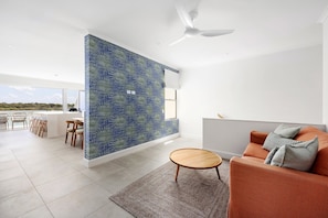 A modern living room with a large window, a ceiling fan, and a seating area with a sofa and chairs.