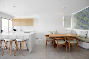 A modern kitchen with white cabinetry, a central island with stools, and a dining area with a wooden table and chairs.