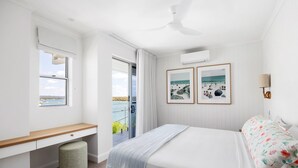 Une chambre à coucher comprenant un lit, un bureau, une chaise, un ventilateur de plafond et une fenêtre donnant sur la mer.