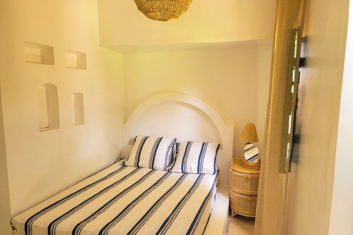Un dormitorio con una cama, una mesita de noche con lámpara y una puerta.