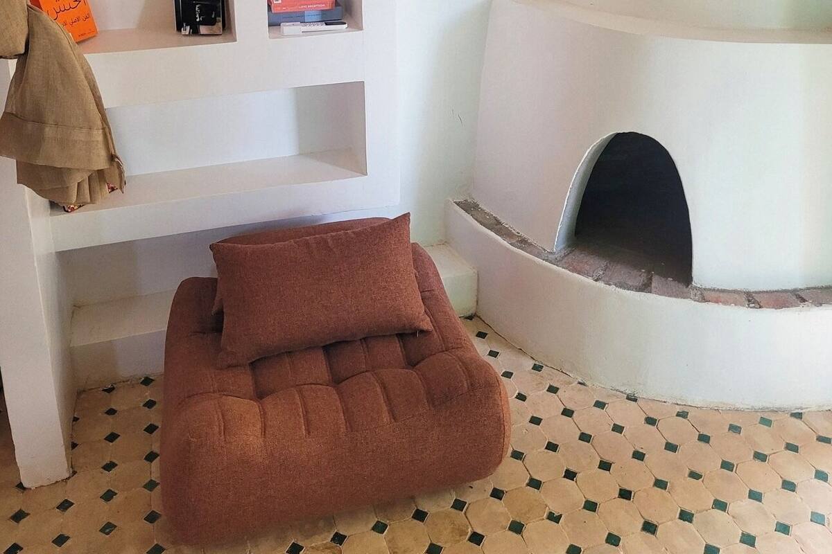 Un salón acogedor con una chimenea blanca, un sofá marrón cómodo y una estantería con libros y objetos decorativos.