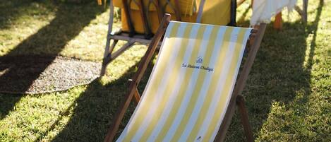 A grassy outdoor area with a yellow and white striped lounge chair and a table with a white tablecloth.