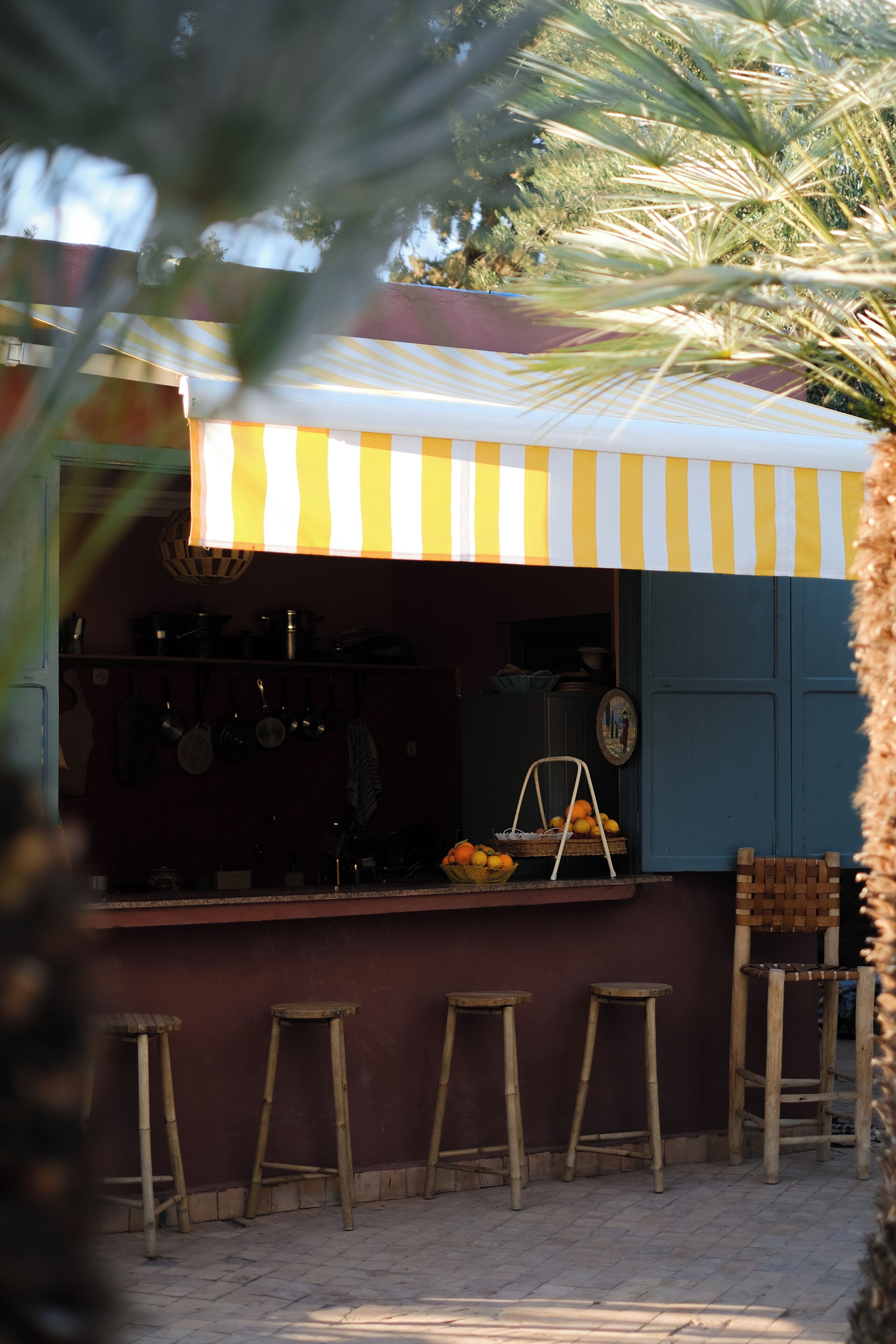Un bar rústico al aire libre con toldo a rayas, taburetes de madera y una palmera en primer plano.