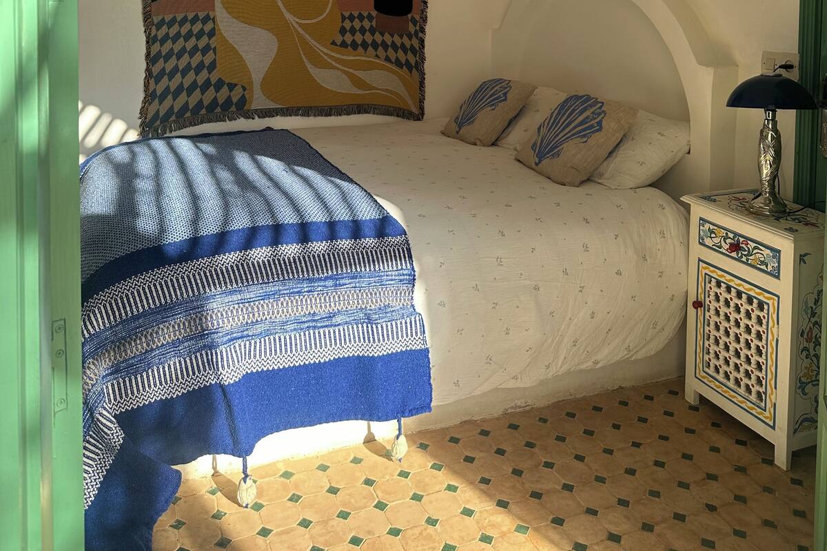 Un dormitorio con una cama, una lámpara colgante, un tapiz y un suelo estampado.