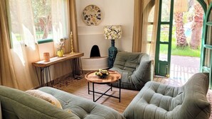 A cozy living room with a green sofa set, a wooden coffee table with fruit, and a decorative plate on the wall. - Maison Chaliya guesthouse  (Tamazouzte)
