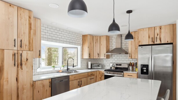 A modern kitchen with wooden cabinets, a white marble island, stainless steel appliances, and pendant lighting.