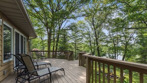 A wooden deck with outdoor furniture, overlooking a forested area and a body of water.