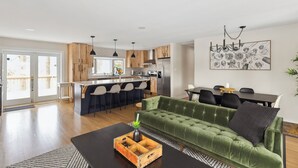 A modern kitchen with wooden cabinets, a dining area with a green sofa, and a bar with stools.