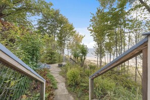 A pathway leading to a beach with a wooden railing on one side and a metal fence on the other, surrounded by greenery.