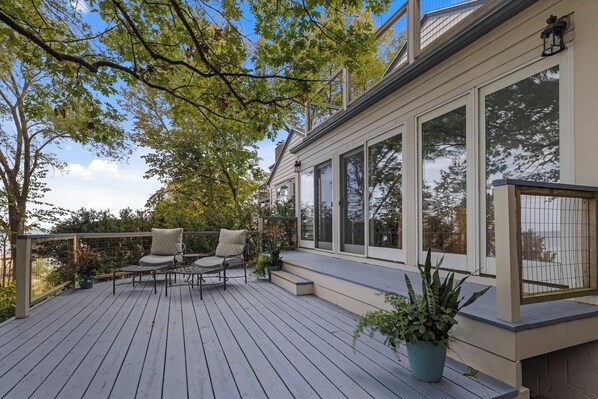 A wooden deck with outdoor seating, large windows, and potted plants.
