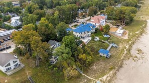 An aerial view of a coastal property with multiple buildings, a large house with a blue roof, and a beach area.