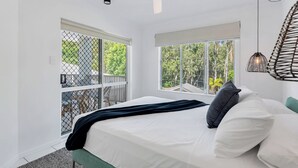 A bedroom with a bed, a ceiling fan, two windows, and a view of greenery outside.