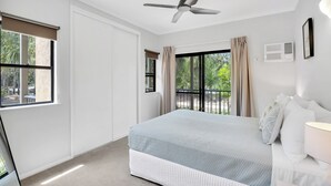 A bedroom with a bed, a ceiling fan, a window with curtains, and an air conditioning unit.