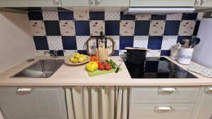 Una cucina con lavello, fornello e piano di lavoro con tagliere, verdure e pentola.