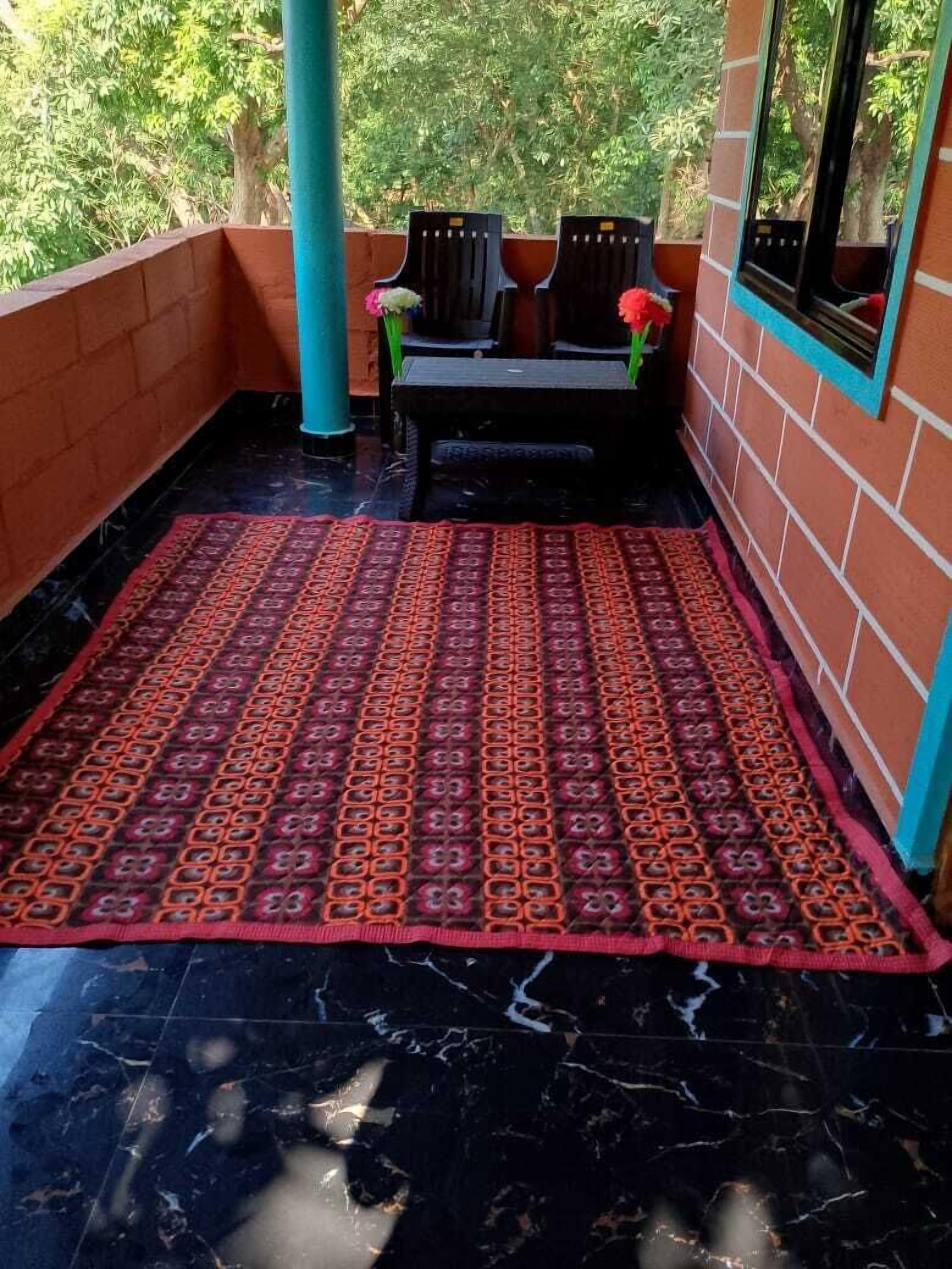 Un espacio de estar al aire libre techado con un tapete estampado, sillas y un banco.