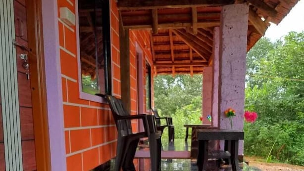Um espaço coberto ao ar livre com piso de mármore preto refletivo, uma mesa com cadeiras e vista para o verde.