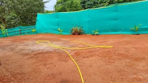 Uma quadra de tênis com uma linha divisória amarela, cercada por uma rede verde e uma superfície de terra batida.
