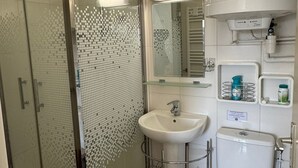 Ein modernes Badezimmer mit Duschkabine aus Glas, einem weißen Waschbecken, einem Spiegel und einer Toilette.