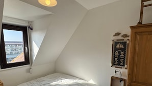 Ein Schlafzimmer mit schrägem Dach, einem Bett, einem Fenster und einer Wandablage mit Dekoration.