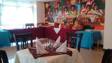 Un comedor con mesas dispuestas para cuatro personas, sillas y un gran mural en la pared.