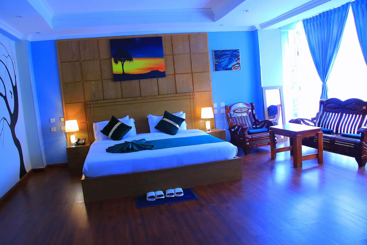 A hotel room with a large bed, bedside lamps, a wooden headboard, a painting, a chair, and a table.