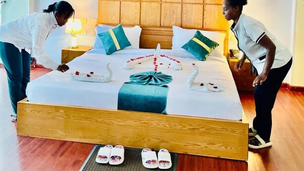 Quarto de hotel com cabeceira de madeira, cama com roupa de cama branca, almofadas verde-água e verdes, e um quadro de um cavalo na parede.