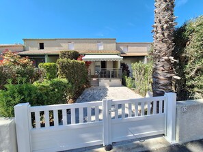 A residential building with a gated entrance, a covered porch, and a well-maintained garden with various plants and a palm tree.