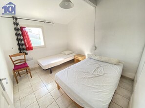 Ett litet, rent rum med en säng, en stol, ett nattduksbord och ett fönster med gardiner.
