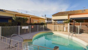 Une piscine entourée d’une clôture en métal, elle-même bordée de bâtiments aux toits recouverts de tuiles.