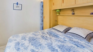 Une chambre à coucher avec un lit, une armoire en bois, un tableau encadré au mur et une petite étagère avec une lampe et des objets décoratifs.