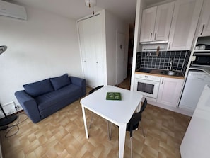 A compact living space with a sofa, a dining table, a kitchenette, and a white wall.
