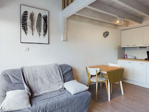 A modern living room with a grey sofa, a wooden dining table, and a kitchen area with white cabinets.