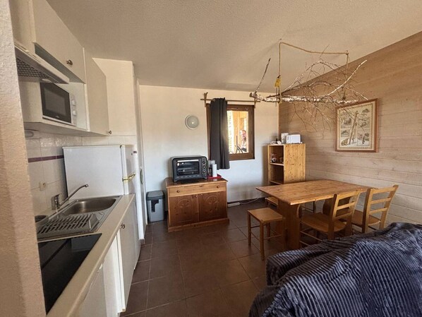 Una cocina compacta con microondas, tostadora y lavamanos. Hay una mesa de comedor de madera con sillas y una ventana con vistas.