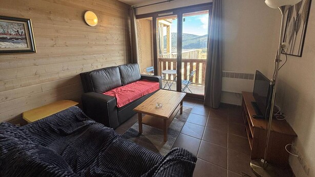 A cozy living room with a sofa, a coffee table, and a TV stand. There is a balcony with a view of the outdoors.