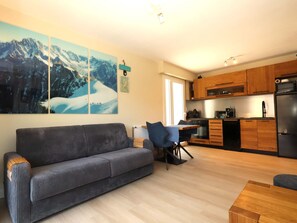 A modern living room with a sofa, a dining table, and a kitchen area with wooden cabinets and appliances.