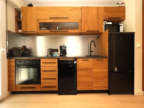 Una cucina con mobili in legno, una lavastoviglie nera, un frigorifero nero e una macchina per il caffè.