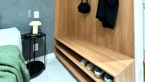 Una habitación moderna con un armario de madera, una mesita de noche con lámpara y una cama con manta verde.