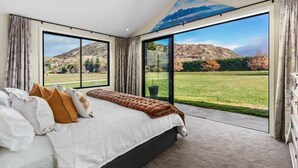 A bedroom with a large bed, a view of a grassy field, and a mountain in the distance.