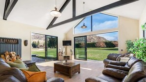 A spacious living room with leather sofas, a wooden coffee table, and large windows offering a view of a mountainous landscape.