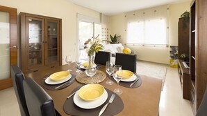 Un coin repas avec une table dressée pour quatre personnes, des chaises, un buffet aux portes vitrées et une fenêtre avec des stores.
