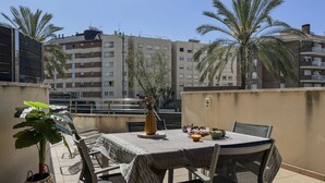 Une terrasse sur le toit, avec une table dressée pour le dîner, entourée de chaises, d’une plante en pot et d’un vase rempli de fleurs.